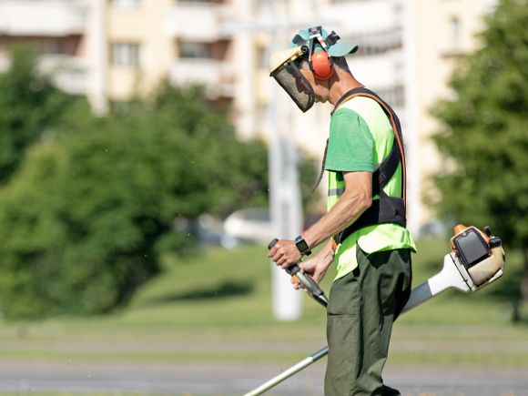 Male dressed in high-vis safety gear strimming a grassed area on an estate