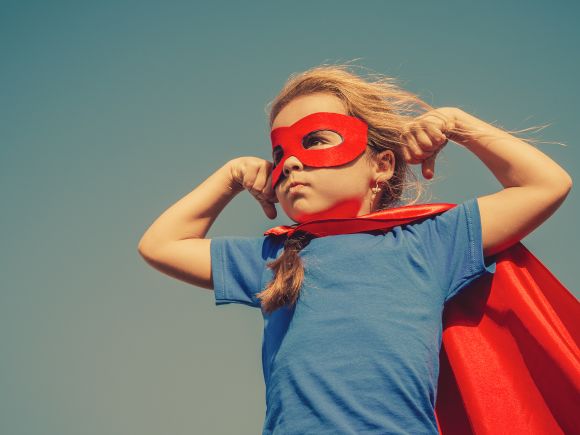 Young girl with blond hair, dressed up in a superheros red cape and mask