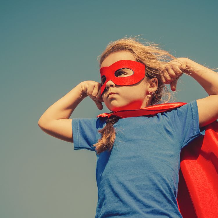 Young girl with blond hair, dressed up in a superheros red cape and mask