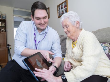 Men in blue shirt showing a lady in yellow how to use a tablet